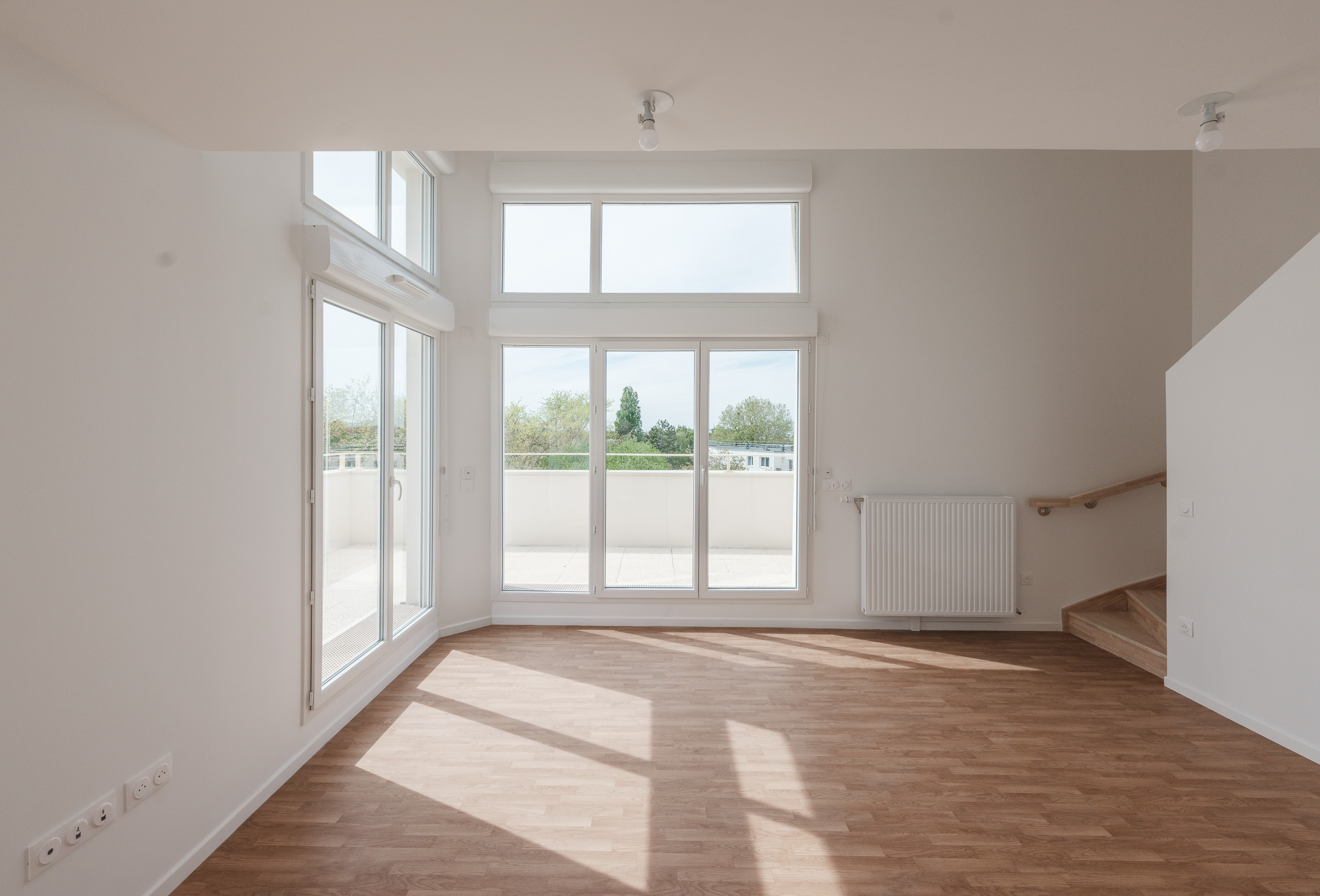 Intérieur d'un logement collectif contemporain aux Clayes-sous-Bois, avec séjour en double hauteur, grandes baies vitrées et terrasse offrant une forte luminosité naturelle.